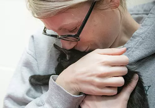 Woman with glasses hugging a dark grey cat